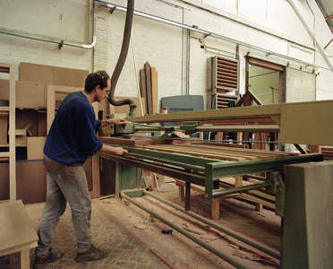 822287 Afbeelding van een werknemer bezig aan een zaagmachine in de werkplaats van Aannemingsbedrijf H.J. Jurriëns ...